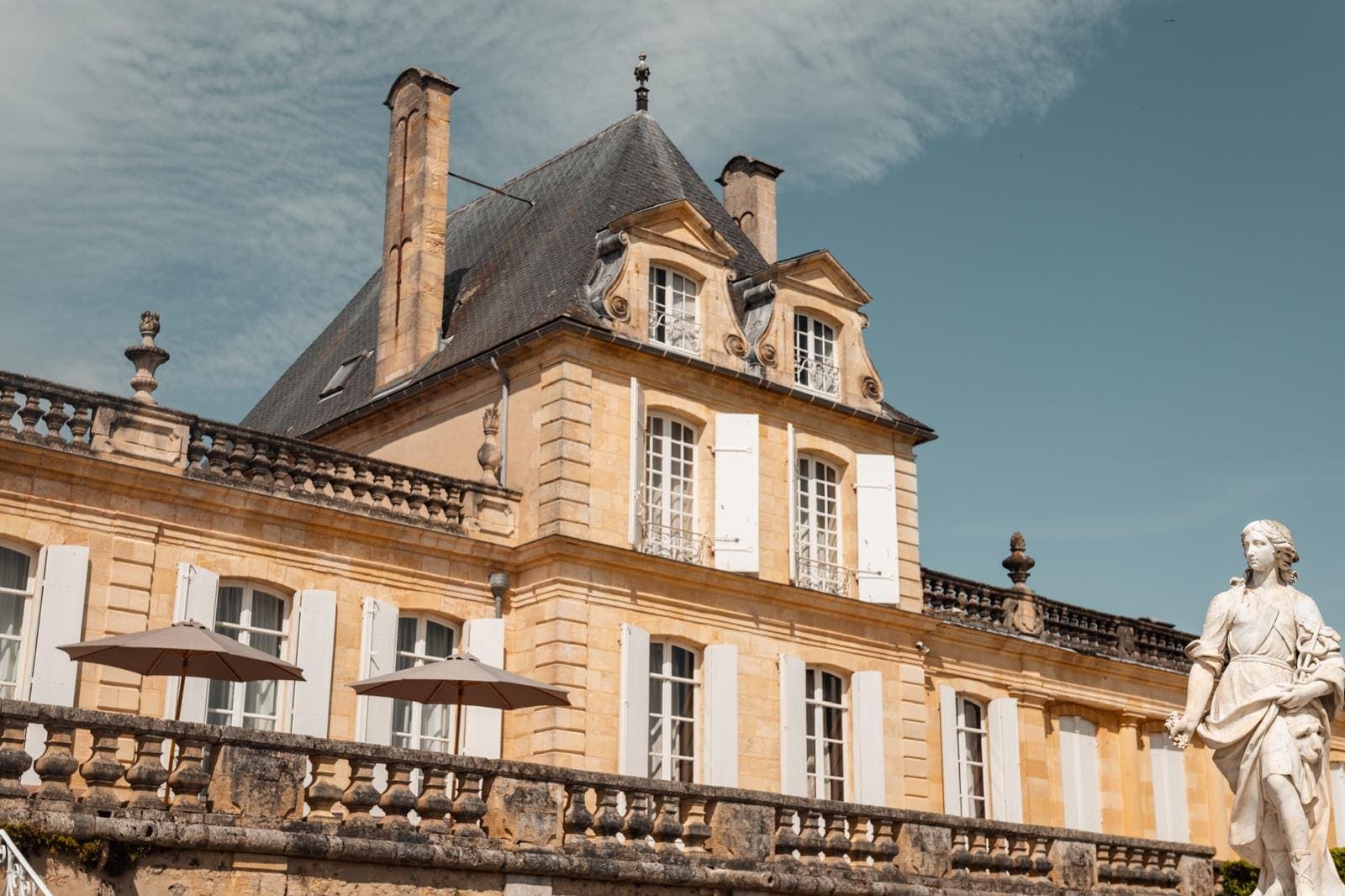 Façade classique d'un château bordelais au toit à la Mansart, terrasse à balustrade et statue au premier plan